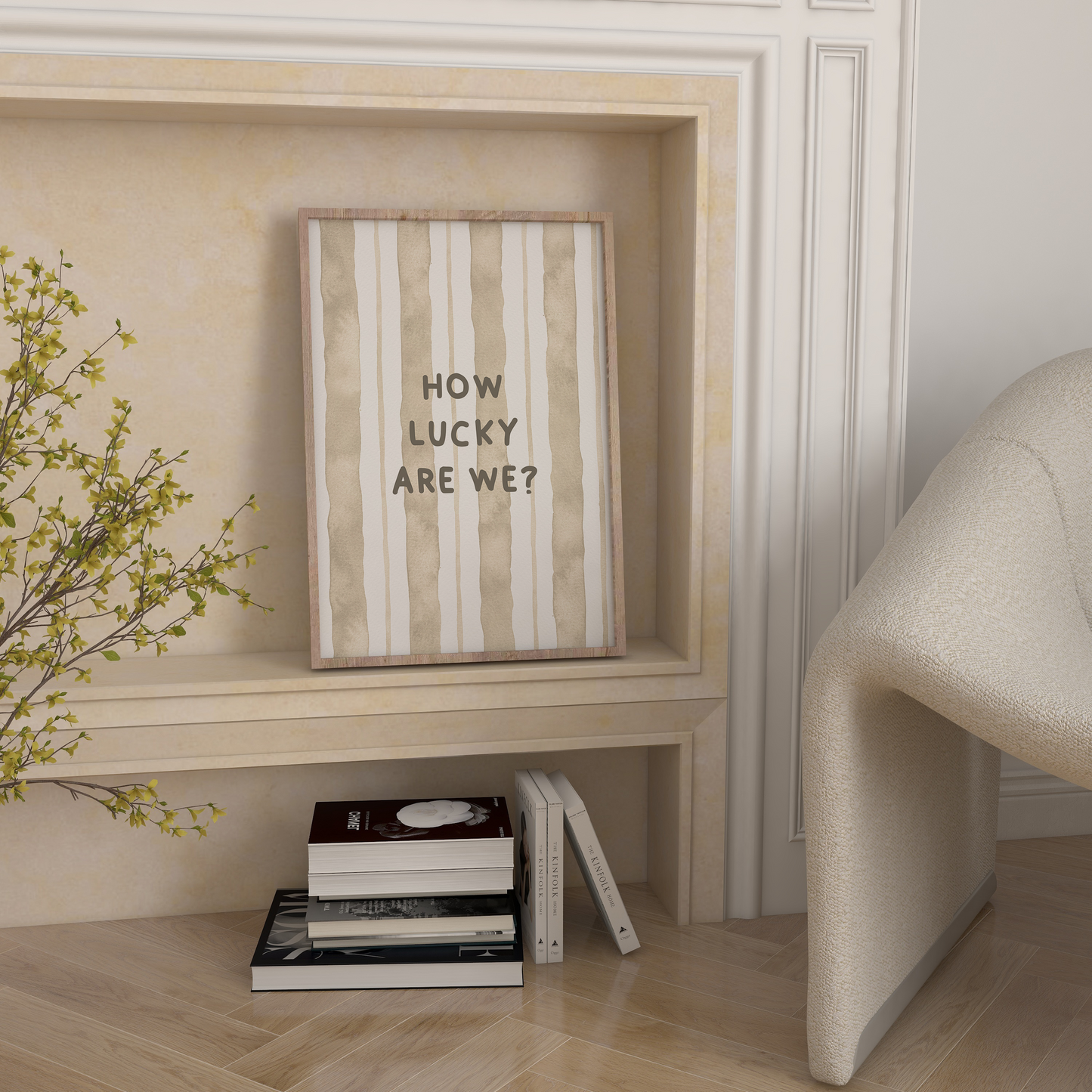 Framed picture with 'How Lucky Are We?' text on a wall with books and a plant below.