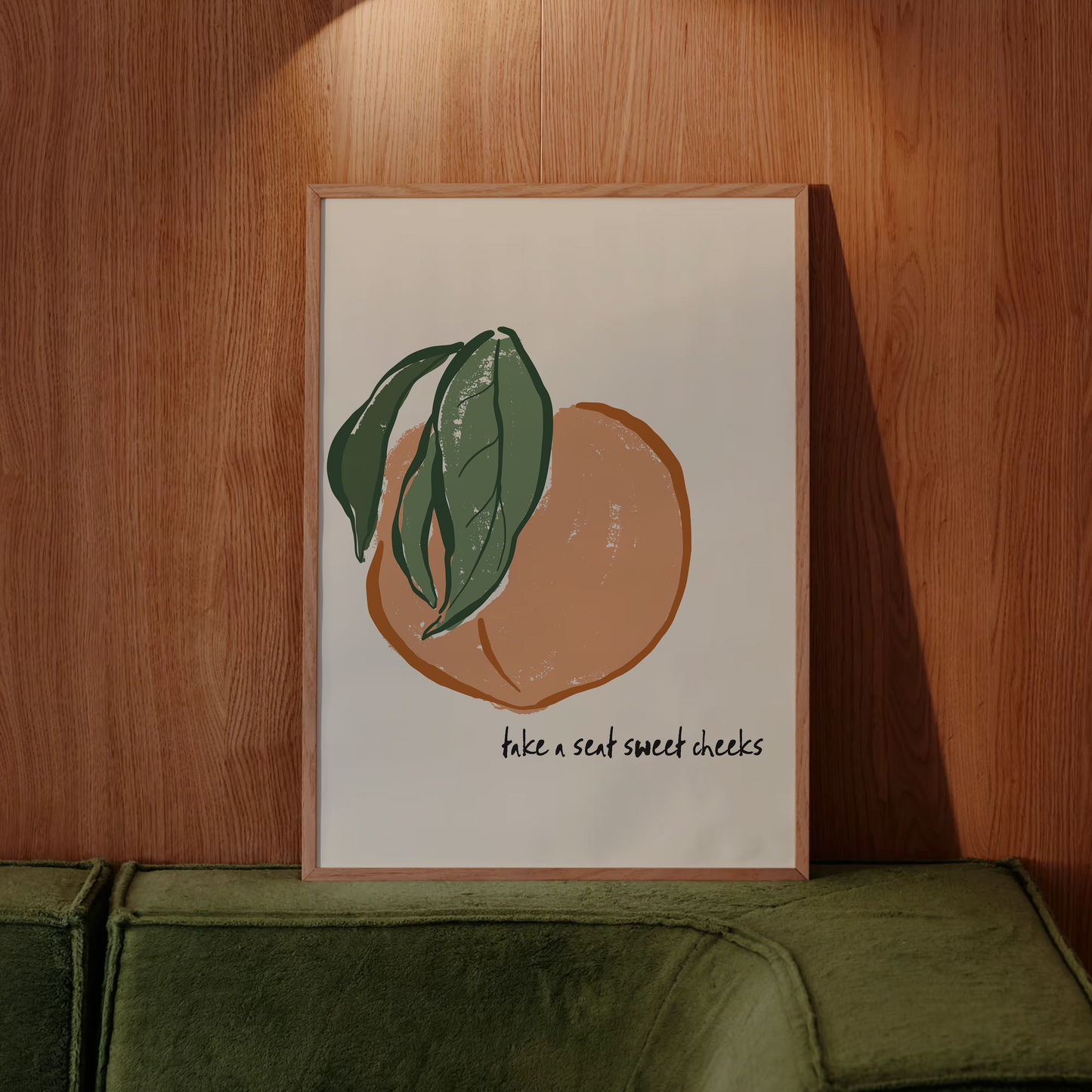 Framed artwork of a peach with leaves on a wooden wall above a green sofa.