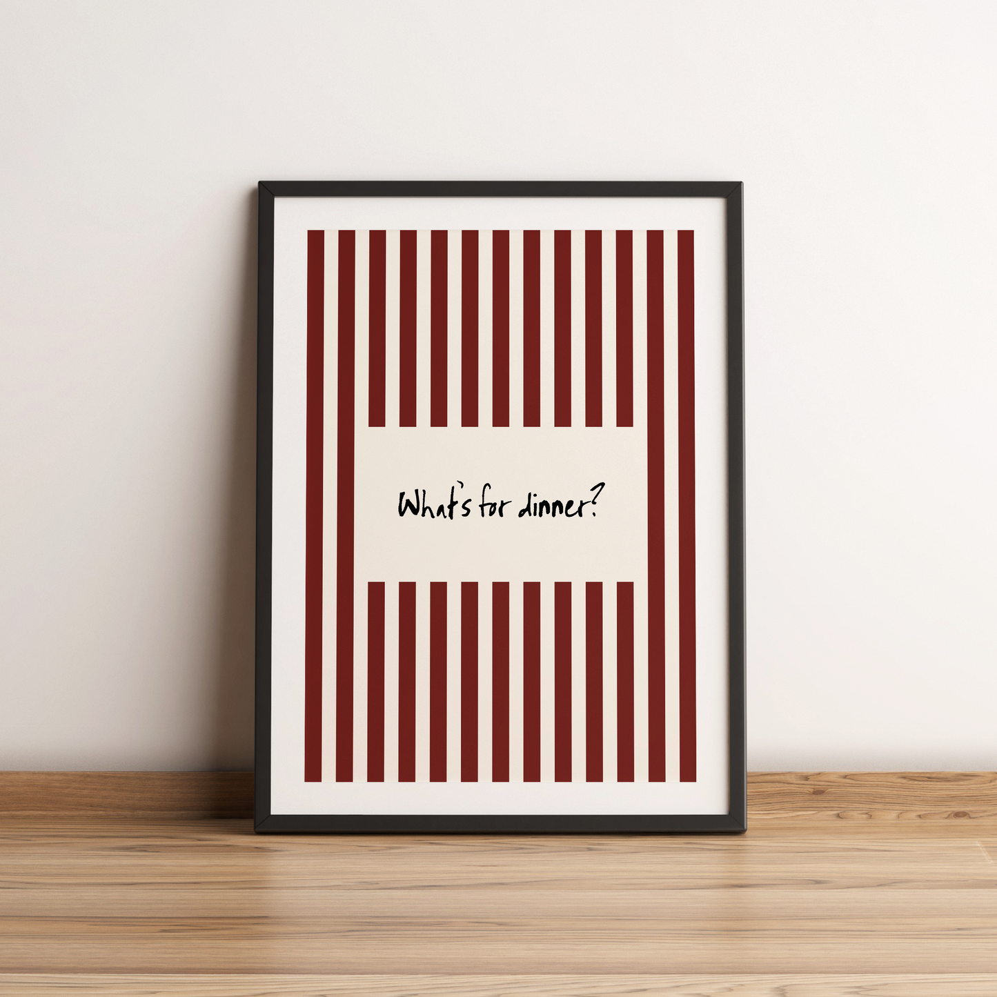 Framed poster with red and white striped design and text 'What's for dinner?' on a wooden surface.