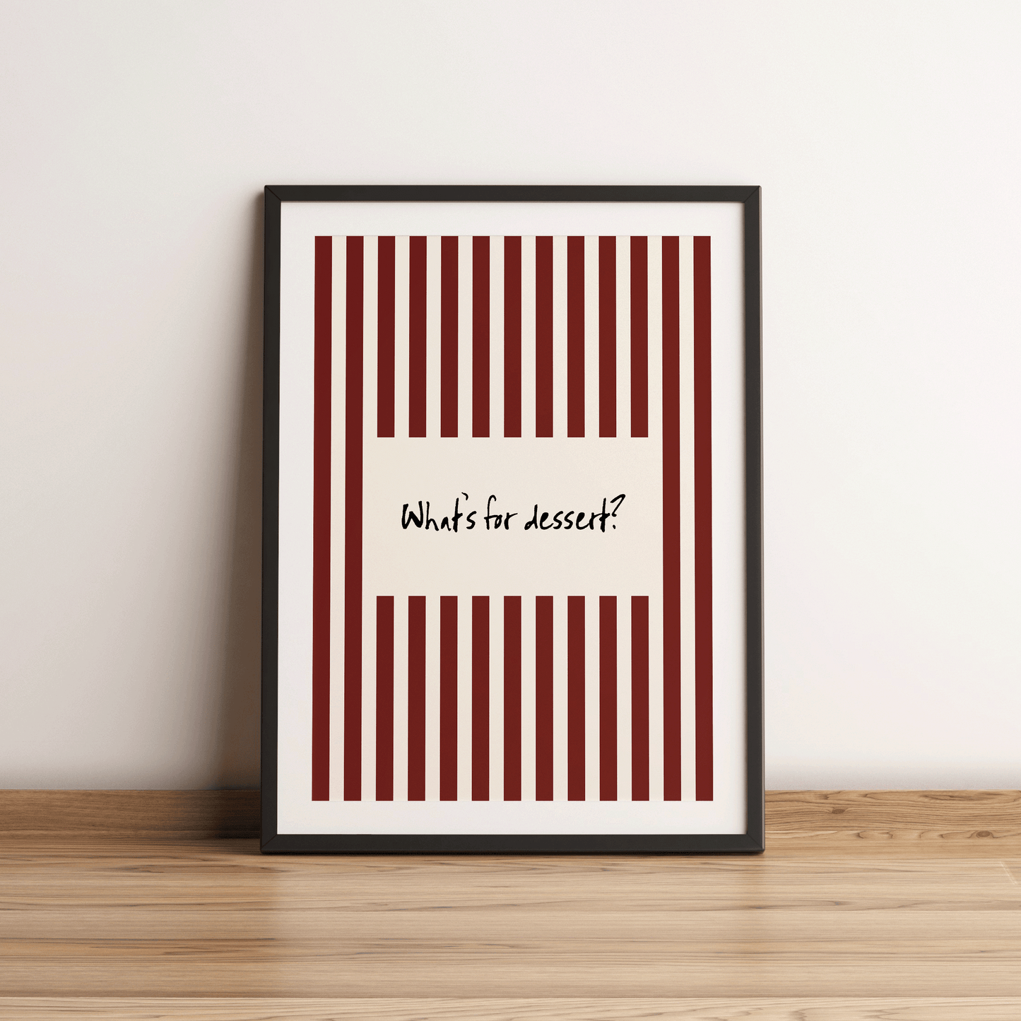 Framed poster with red and white striped design and text 'What's for dessert?' on a wooden surface.