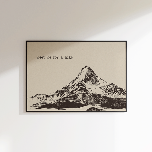 Framed print of a mountain with 'meet me for a hike' text on a white wall.
