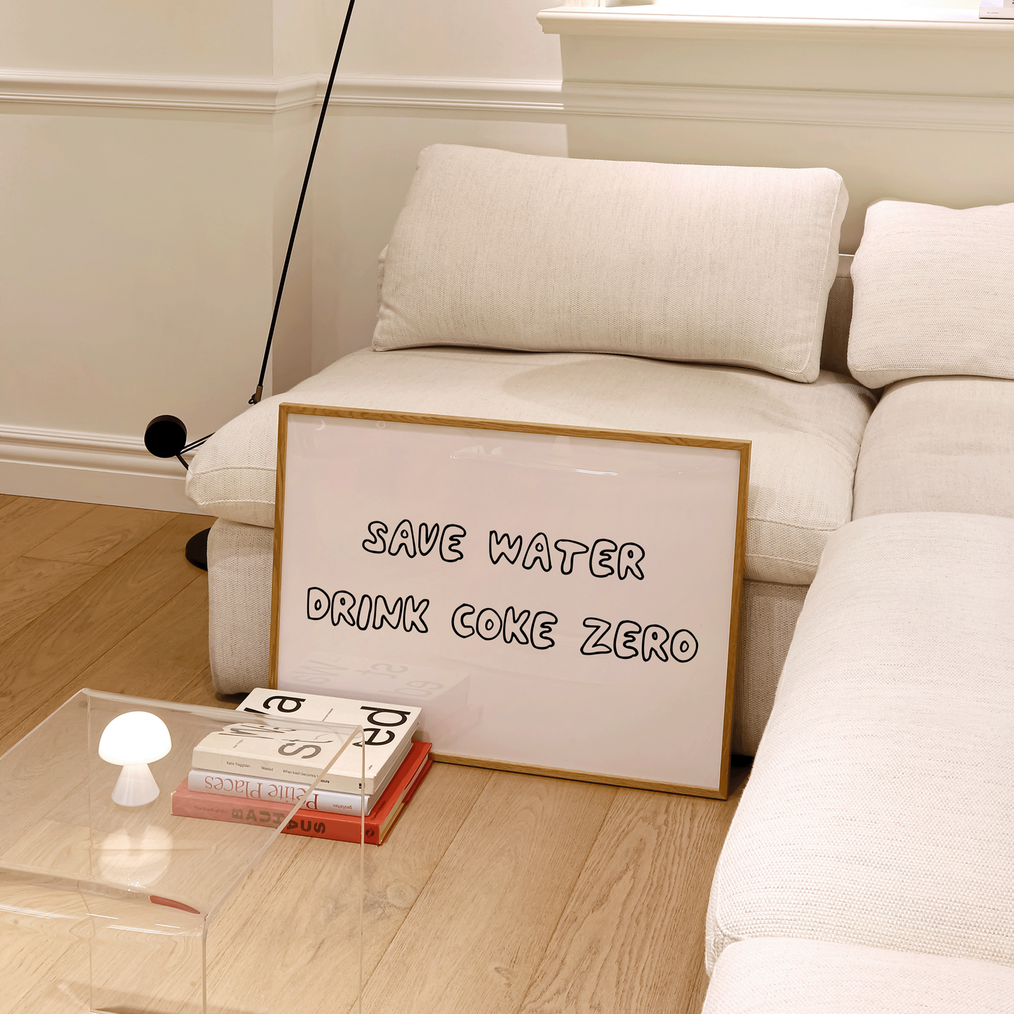White sofa with a framed sign reading 'Save water, drink Coke Zero' in a room with a lamp and coffee table.