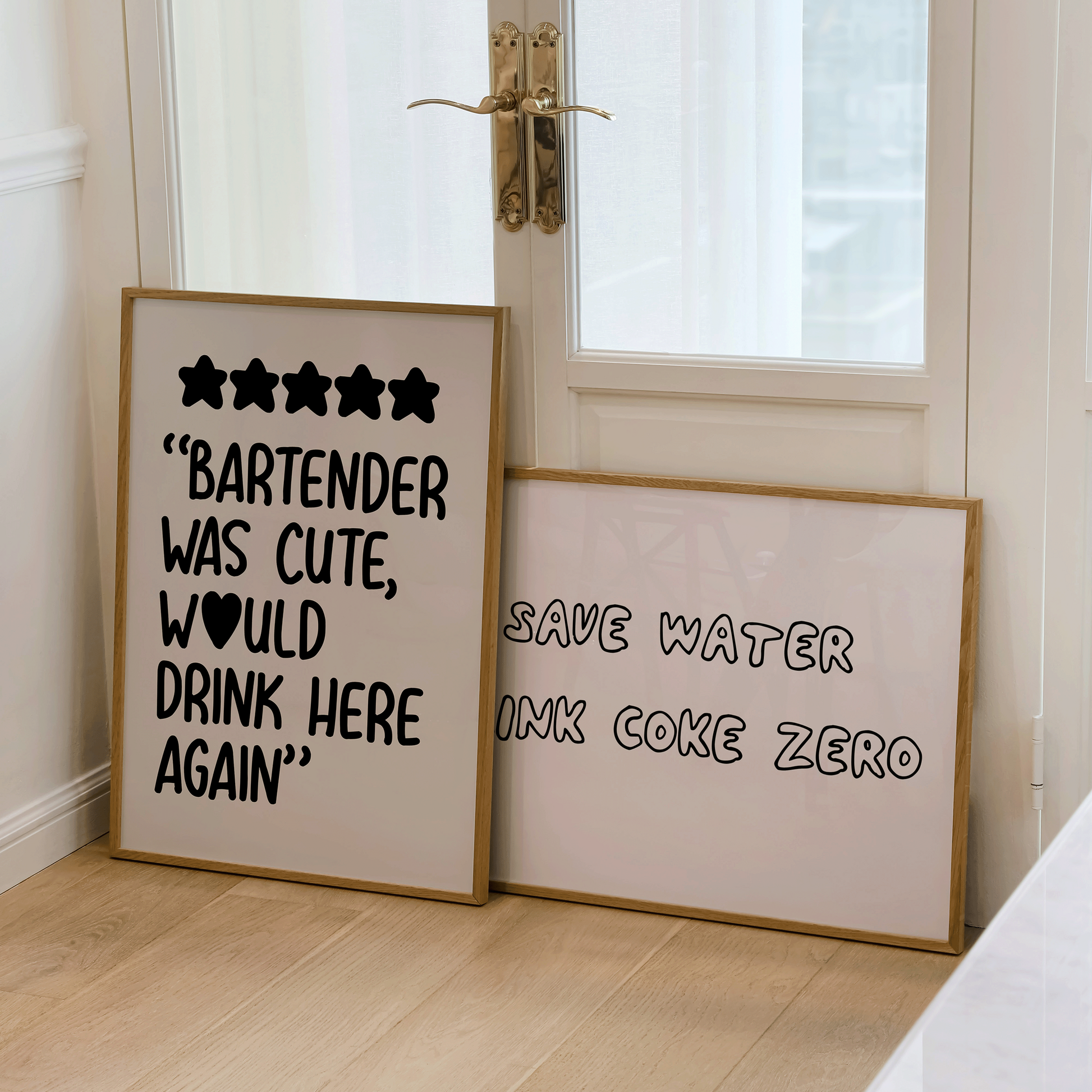 Two framed prints on a wooden floor with a glass door in the background.