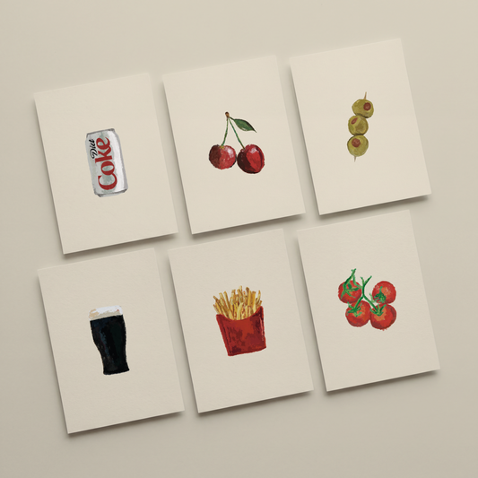 Six square cream art prints arranged in a 2x3 grid on a light beige wall. Each print features a different watercolor-style food or drink illustration: a Coke can, two red cherries, three green olives, a dark beer glass, a red french fries container with yellow fries, and red tomatoes with green stems.