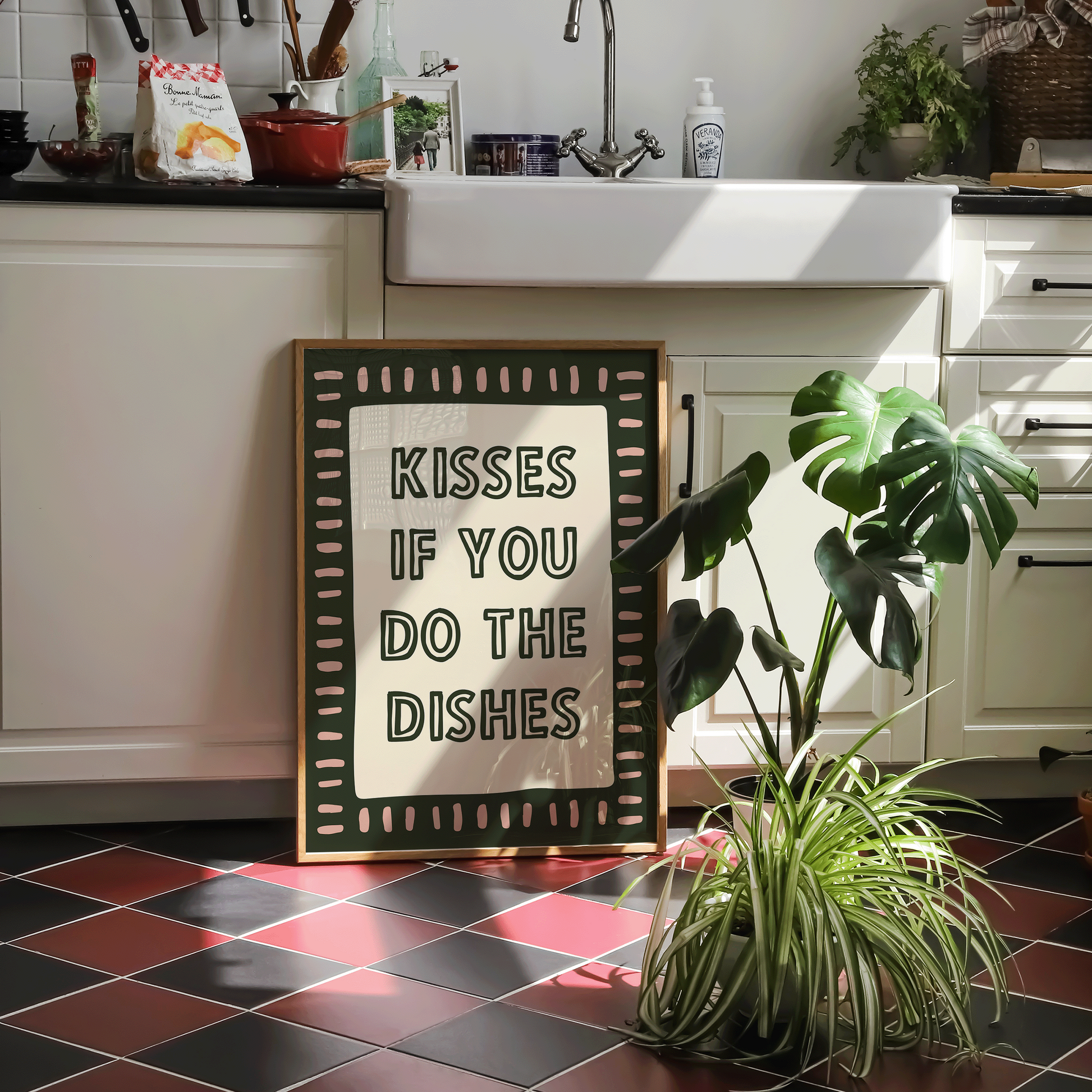 Kitchen with checkered floor, plant, and framed sign reading 'Kisses if you do the dishes'.