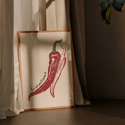 Framed artwork of a red chili pepper on a white background, leaning against a curtain.