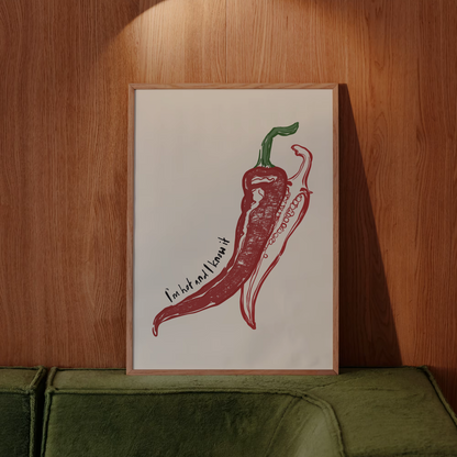 Framed artwork of a red chili pepper on a wooden wall above a green sofa.